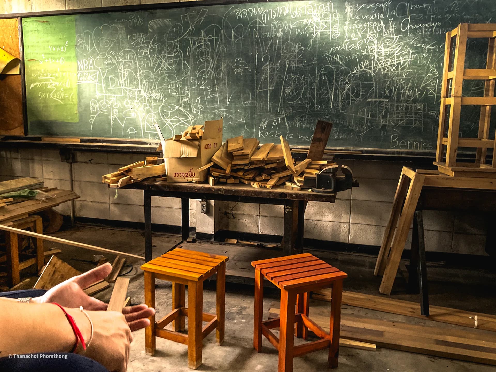 Woodworking classroom with a chalk-covered blackboard, timber offcuts, and two finished stools
